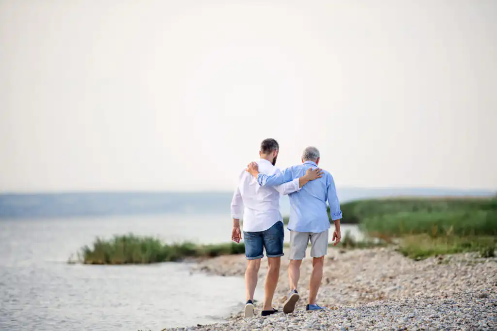 Rear view of senior father and mature son walking by the lake. Copy space.